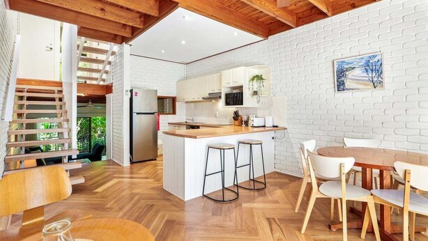 A modern kitchen with white brick walls, wooden beams, and a central island with stools. - Central Noosa location in Noosa Heads (Noosa Heads)
