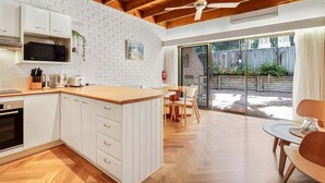 A modern kitchen with white cabinets, a wooden countertop, and a dining area with a table and chairs. - Central Noosa location in Noosa Heads (Noosa Heads)
