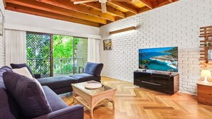A living room with a sofa, television, and wooden flooring. - Central Noosa location in Noosa Heads (Noosa Heads)