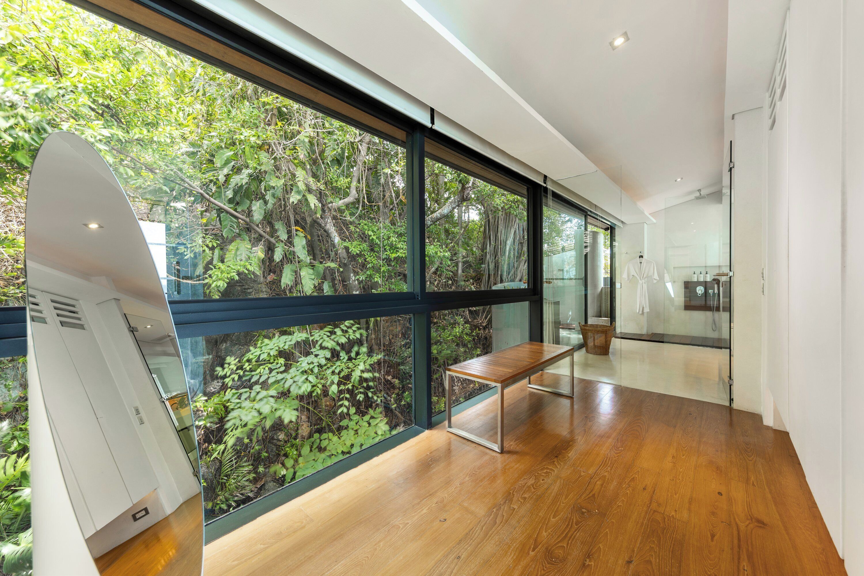 Un intérieur moderne avec de grandes fenêtres, un banc en bois et une porte en verre donnant sur une salle de bain.