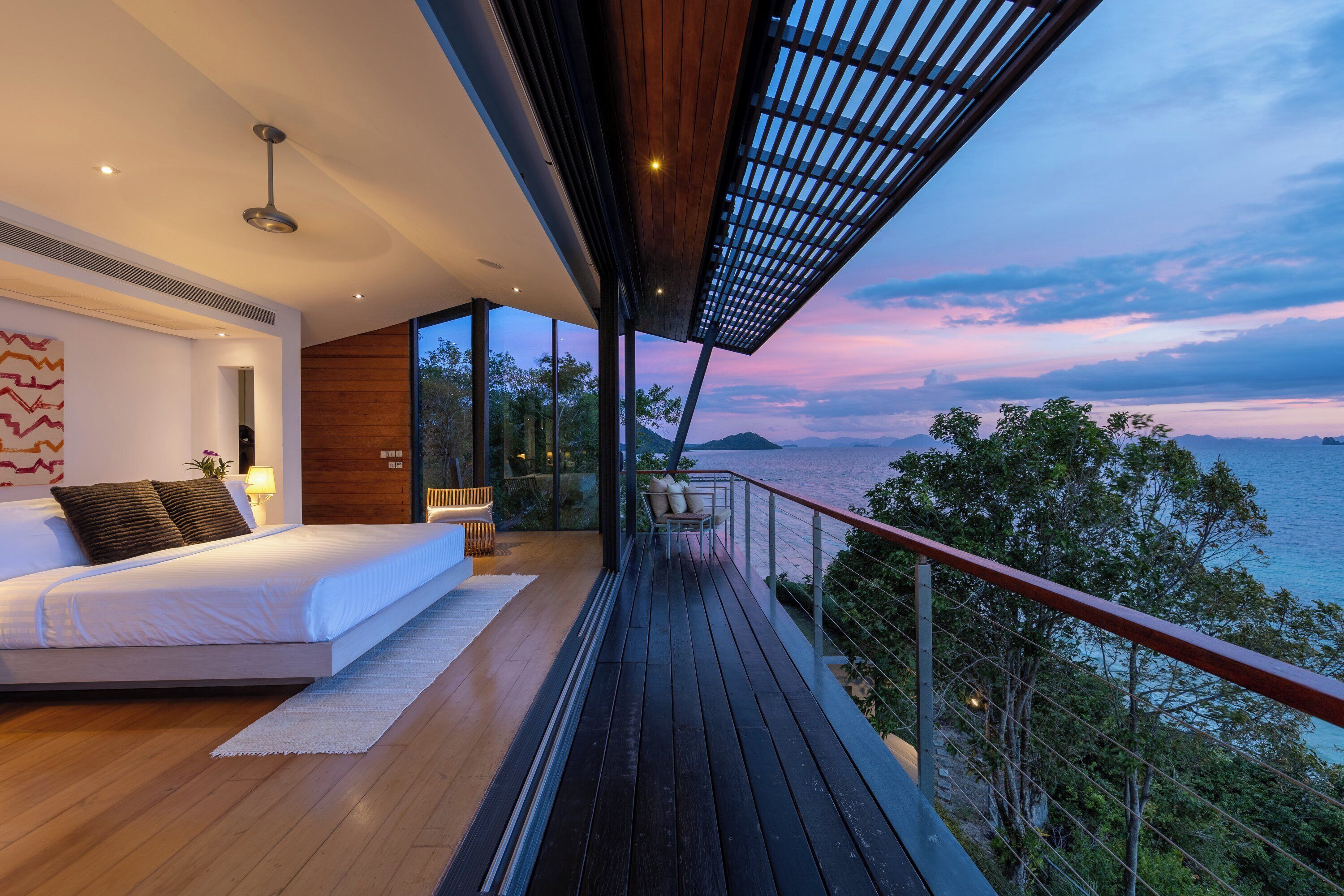 A modern bedroom with a large bed, a view of the sea, and a balcony with a railing.