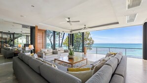 A modern living room with a large gray sofa, a wooden coffee table, and a view of the ocean. - The View (Koh Samui)