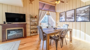 A cozy living room with a fireplace, a flat-screen TV, a dining table with chairs, and framed pictures on the wall. - ★ Summer Ready ★ Hot Tub, Summit Views, Close to Village (Mammoth Lakes)