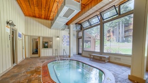A swimming pool with a wooden deck, a bench, and a view of a forested area through large windows. - ★ Summer Ready ★ Hot Tub, Summit Views, Close to Village (Mammoth Lakes)