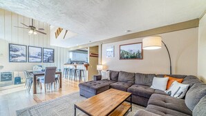 A modern living room with a sectional sofa, a wooden coffee table, and a dining area with a table and chairs. - ★ Summer Ready ★ Hot Tub, Summit Views, Close to Village (Mammoth Lakes)