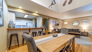 A spacious living area with a wooden dining table, grey sofa, and a kitchen in the background. - ★ Summer Ready ★ Hot Tub, Summit Views, Close to Village (Mammoth Lakes)