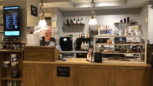 A coffee shop counter with a sign reading "Pay & Order Here," a digital menu board, and shelves stocked with various beverages and condiments.