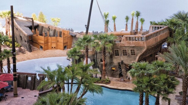 A pool area with a pirate-themed structure, palm trees, and a bridge.