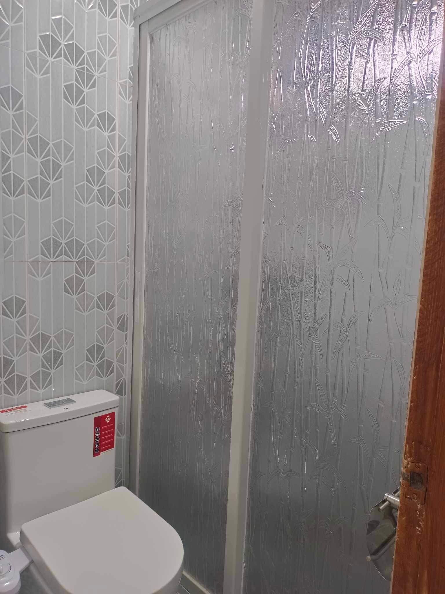 Une salle de bain comprenant des toilettes, un espace douche et un mur décoré d’un motif.