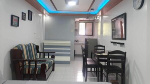 Un espacio habitable compacto con sofá, mesa de comedor, sillas, zona de cocina y un reloj en la pared.