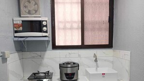 Una cocina compacta con estufa a gas, una cocedora de arroz, microondas y pileta.