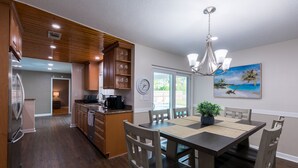 Eine moderne Küche mit Holzausstattung, ein Essbereich mit einer Chandelierleuchtre und ein Gemälde, das eine Strandansicht zeigt.