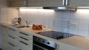 Een moderne keuken met een inbouwoven, roestvrijstalen kastjes en een fruitschaal op het aanrecht.
