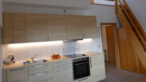 Een moderne keuken met houten kastjes, een ingebouwde oven en een houten trap.