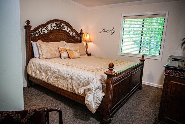 A bedroom with a wooden bed, a bedside lamp, a window with blinds, and a wall with the word "family" written on it. - Stunning wooded view Chalet near our salt water pool! (Pine Mountain)