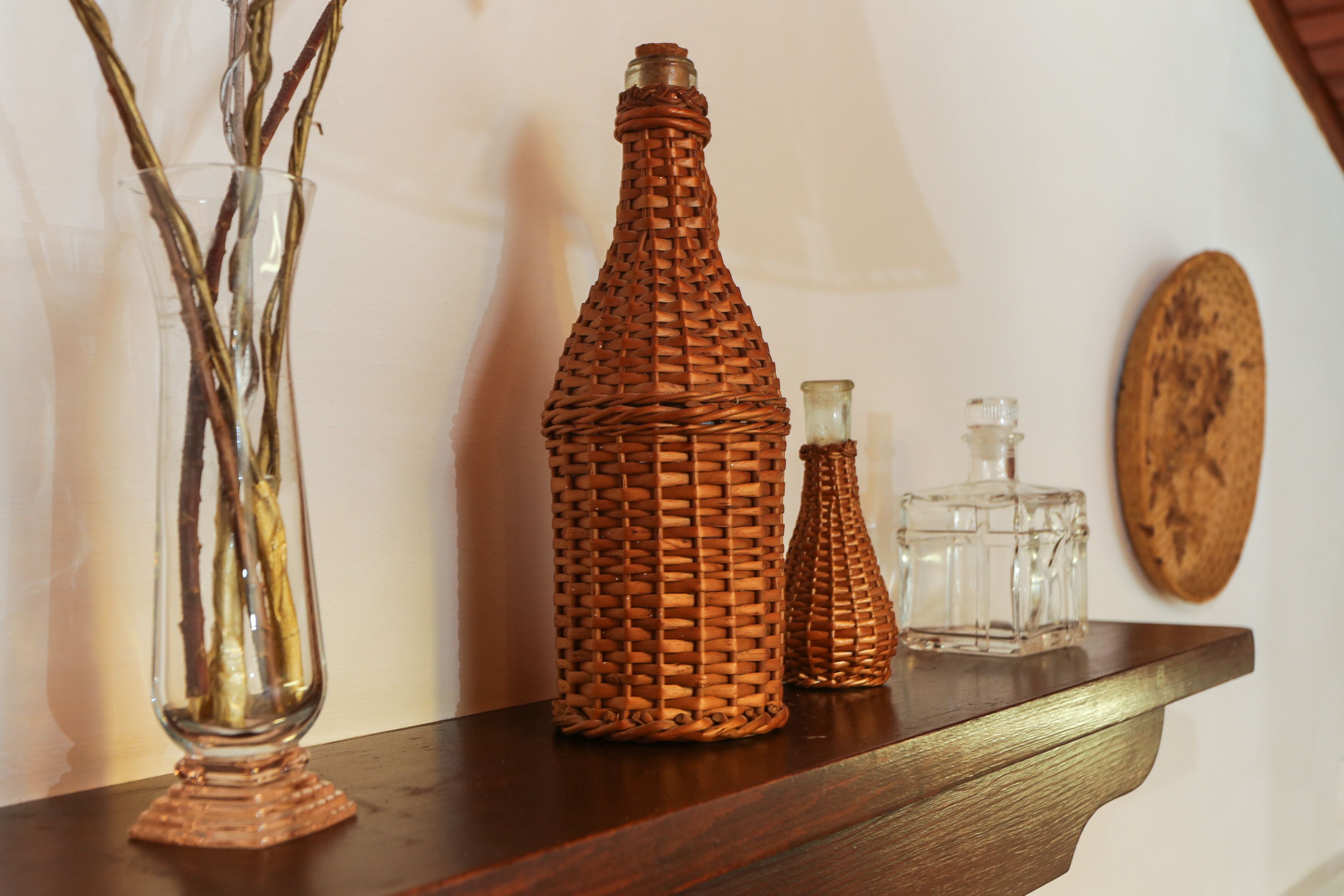 Una estantería de madera con tres botellas de vidrio y un jarrón con ramas.