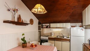 A kitchen with white cabinets, a stove, and a refrigerator. There is a dining table with a pink tablecloth and a basket of fruit. - Apartment Ikana (Dubrovnik)