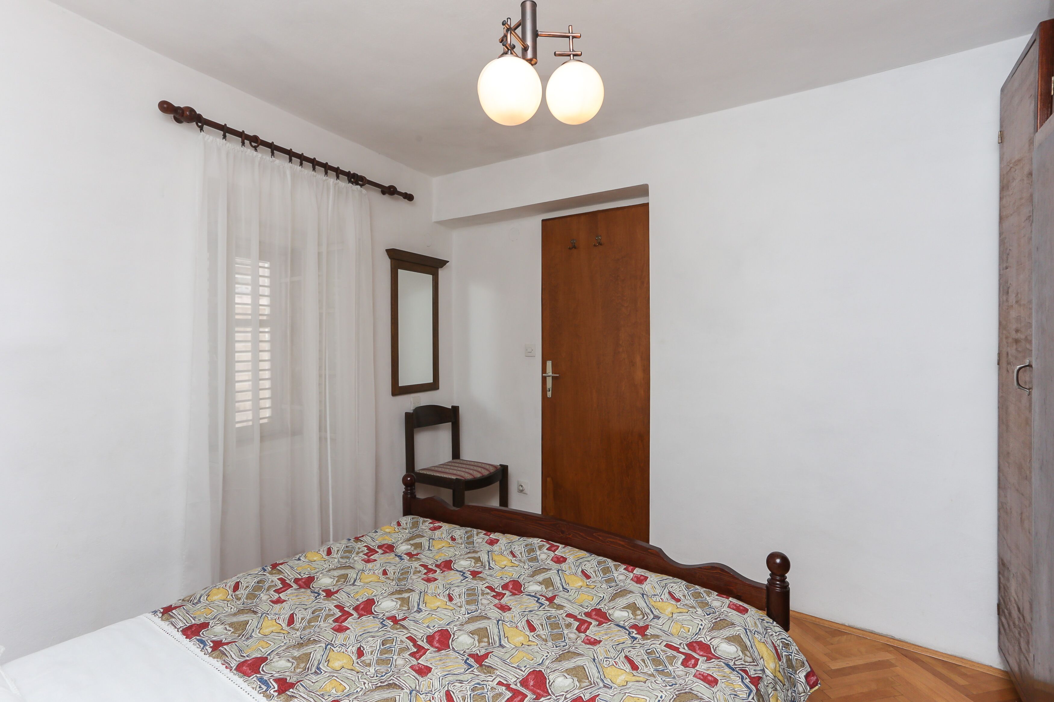 Une chambre avec un lit en bois, une chaise, une porte en bois et un miroir au mur.