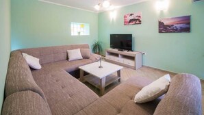 Una sala de estar con un sofá modular, una mesa de centro, un televisor de pantalla plana y obras de arte en las paredes.