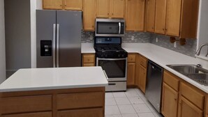 Una cocina moderna con armarios de madera, electrodomésticos de acero inoxidable y encimera blanca.