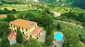 Eine große Villa mit Swimmingpool, umgeben von üppiger Vegetation und Hügeln.