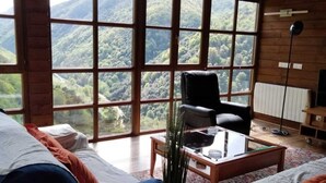 Une pièce confortable avec une grande fenêtre donnant sur les montagnes, un canapé, un fauteuil et une petite table sur laquelle est posé un vase.