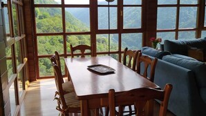 Une table à manger en bois, avec des chaises et un canapé, dans une pièce dotée de grandes fenêtres donnant sur un paysage montagneux.