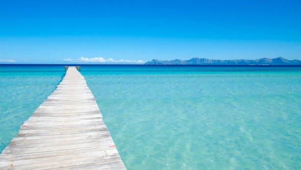 A wooden pier extending into clear turquoise water with a mountain range in the distance. - Beach house for 6 persons, with pool and garden, in Playas de Muro, Mallorca (Muro)
