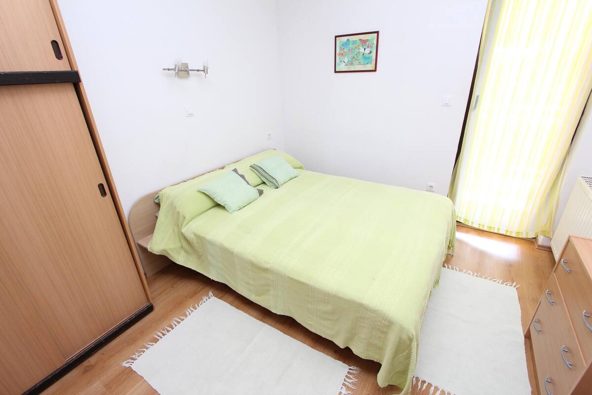 A small, neatly arranged bedroom with a single bed, a wooden wardrobe, and a small cabinet.