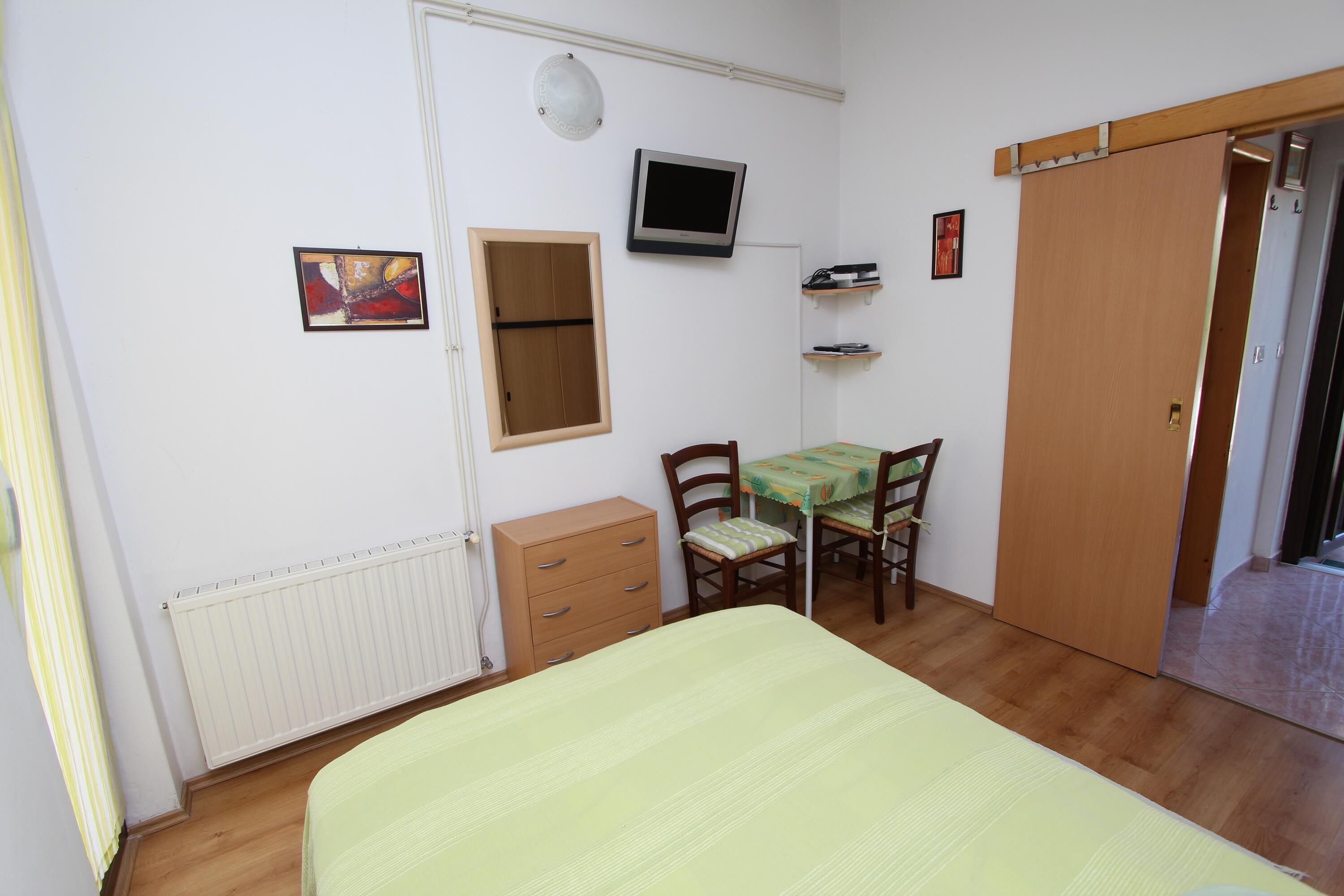 A bedroom with a bed, a desk with a chair, a wardrobe, a radiator, a TV, and a framed picture on the wall.