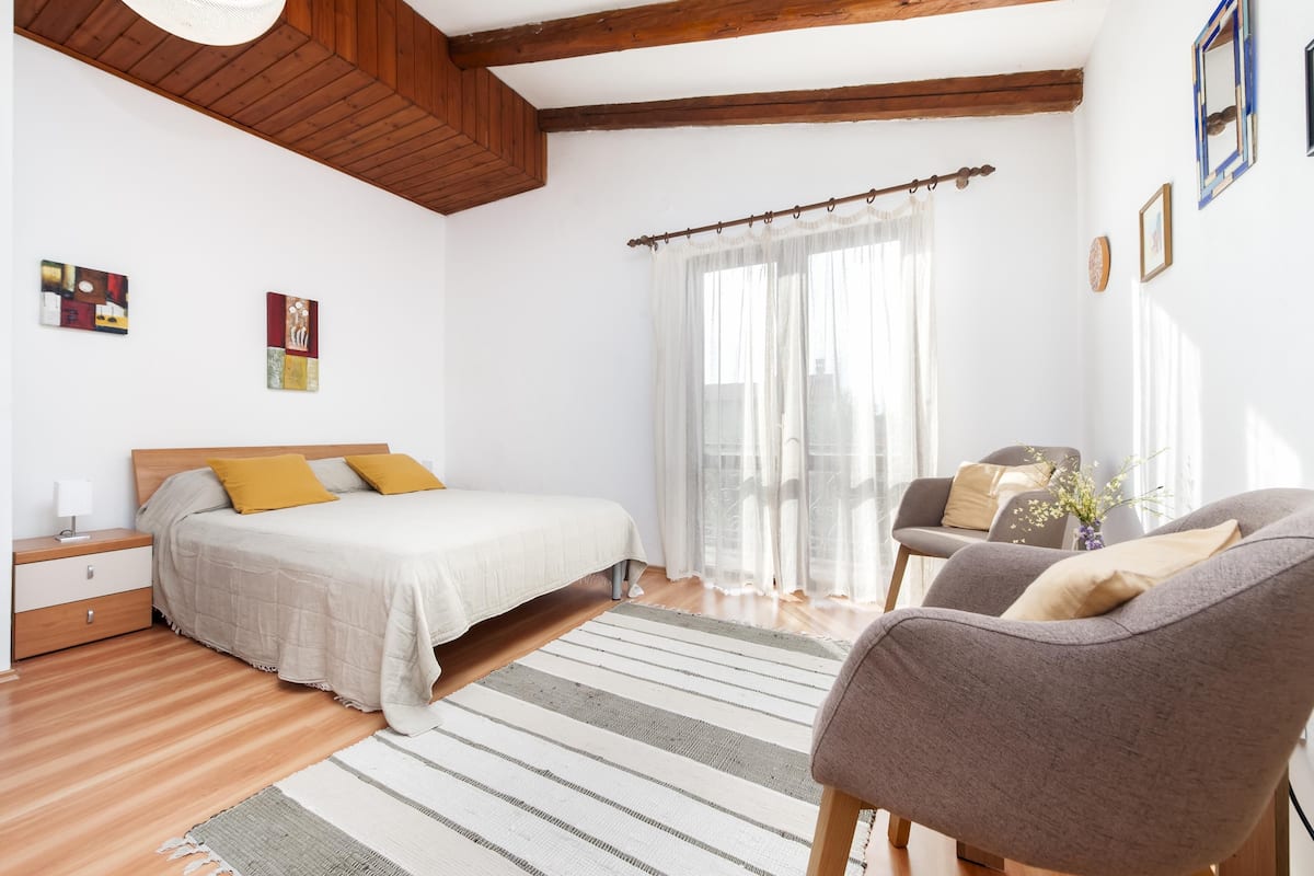 A bedroom with a bed, a chair, a nightstand, and a window with curtains.