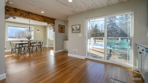 Una habitació àmplia amb sòls de fusta, zona de menjador amb cadires, un penjoll i una gran porta corredissa de vidre que dona a una terrassa exterior amb cadires.