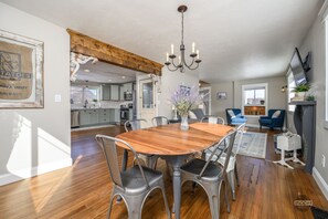 A spacious dining area with a wooden table and metal chairs, a chandelier, and a view into the kitchen. - Revival Acres: Historic Farmhouse on 5 Acres w/Stunning Mountain Views (Palmer)