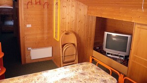 A wooden cabin room with a bed, a small table, a television, and a chair. - Chalet in Carezza al Lago (Carezza Al Lago)
