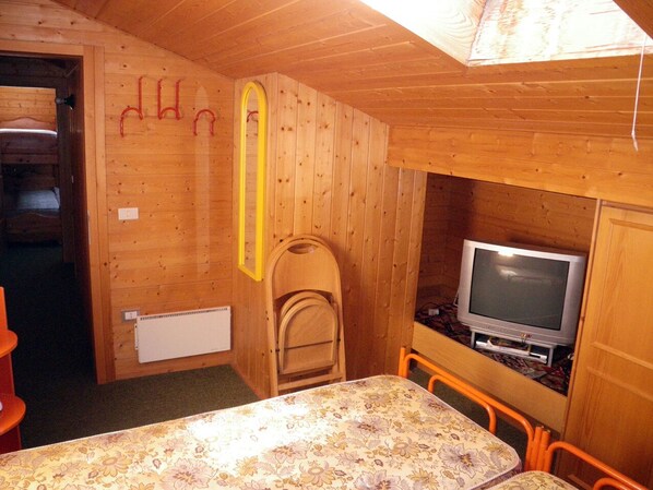 Ein Zimmer in einer Holzhütte mit einem Bett, einem kleinen Tisch, einem Fernseher und einem Stuhl.