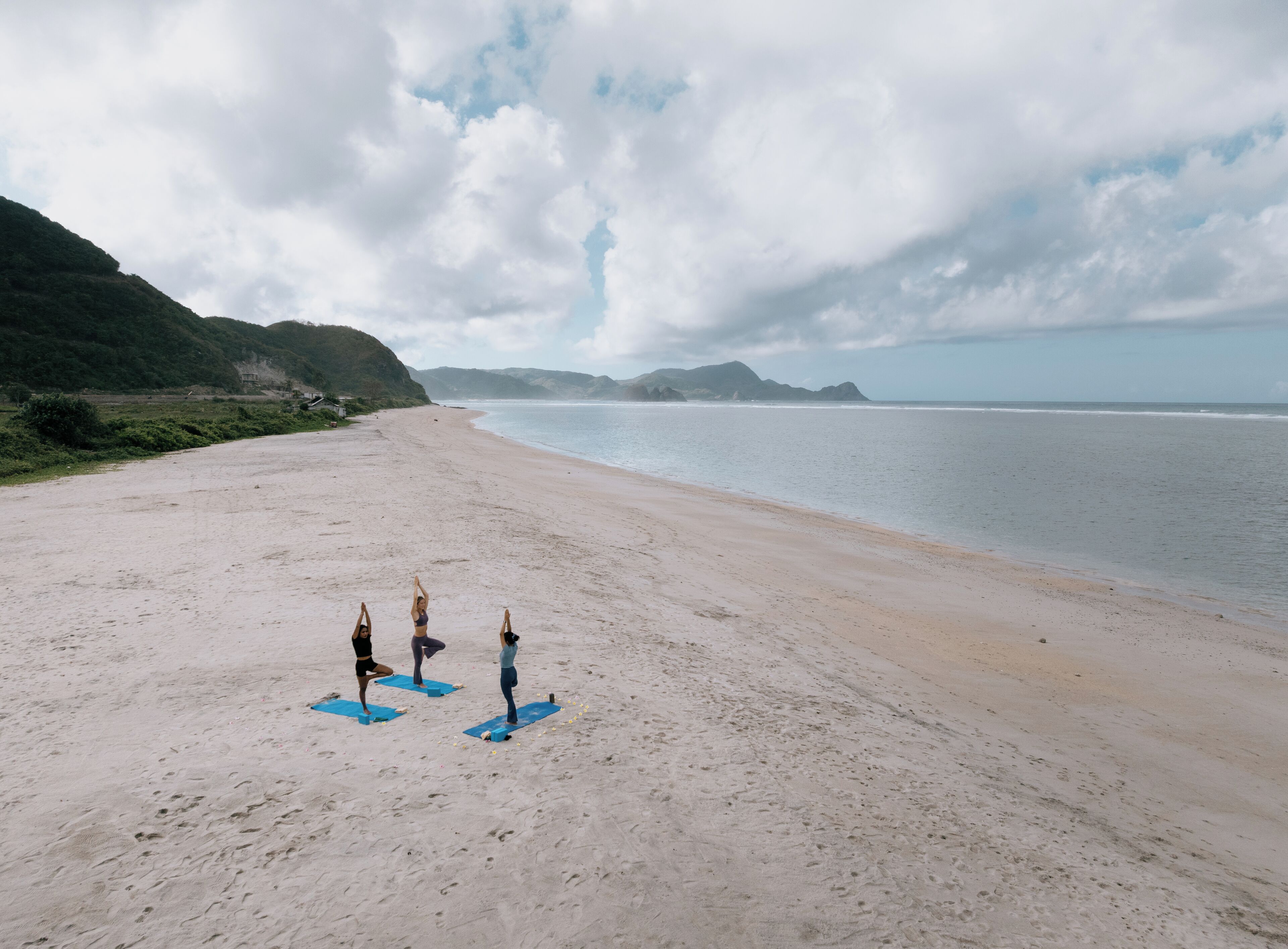 Ein Strand mit drei Personen auf Yogamatten.