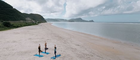 A beach with three people on yoga mats.