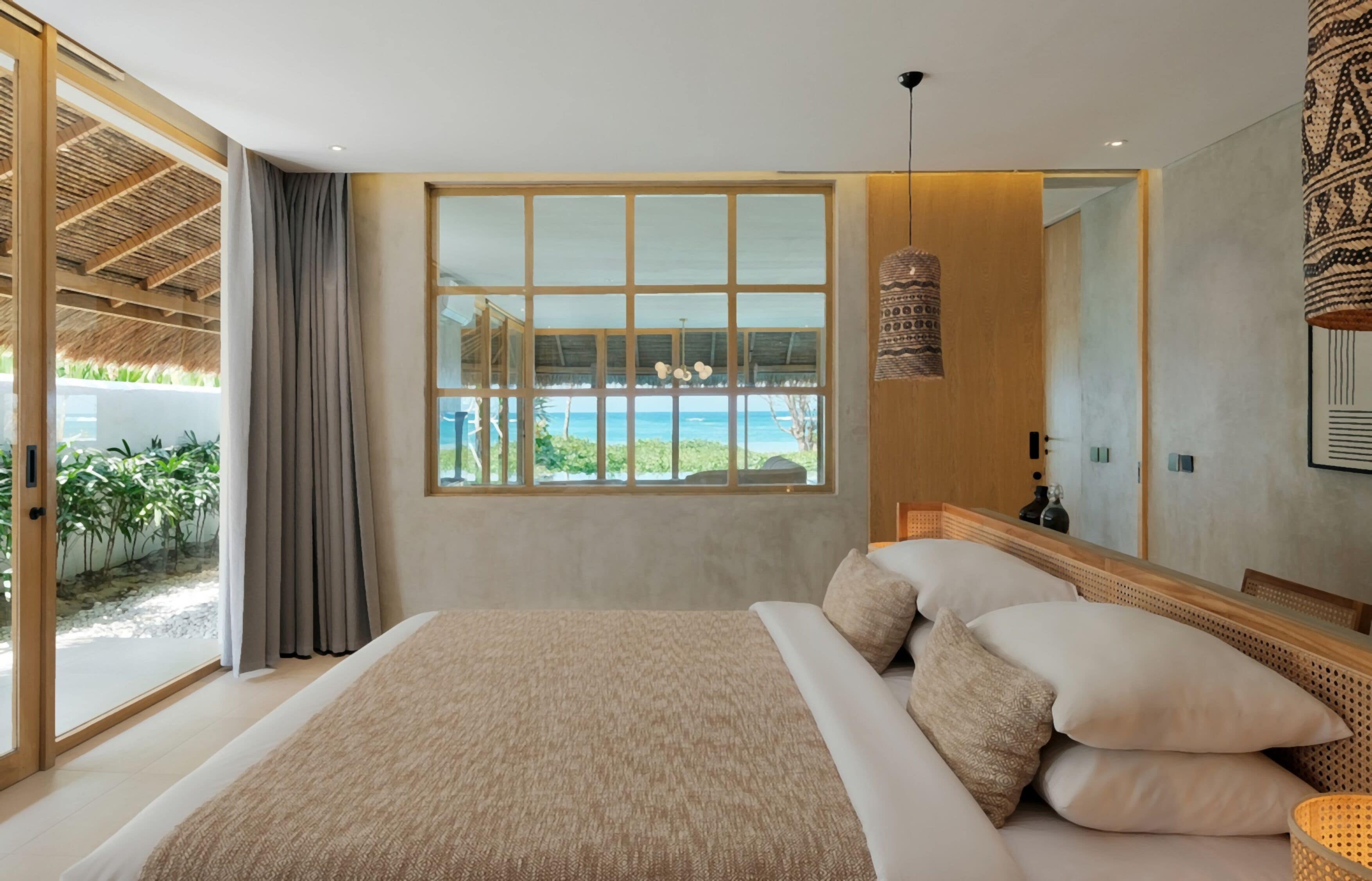 A bedroom with a large bed, a view of the ocean, and a sliding glass door leading to a balcony.