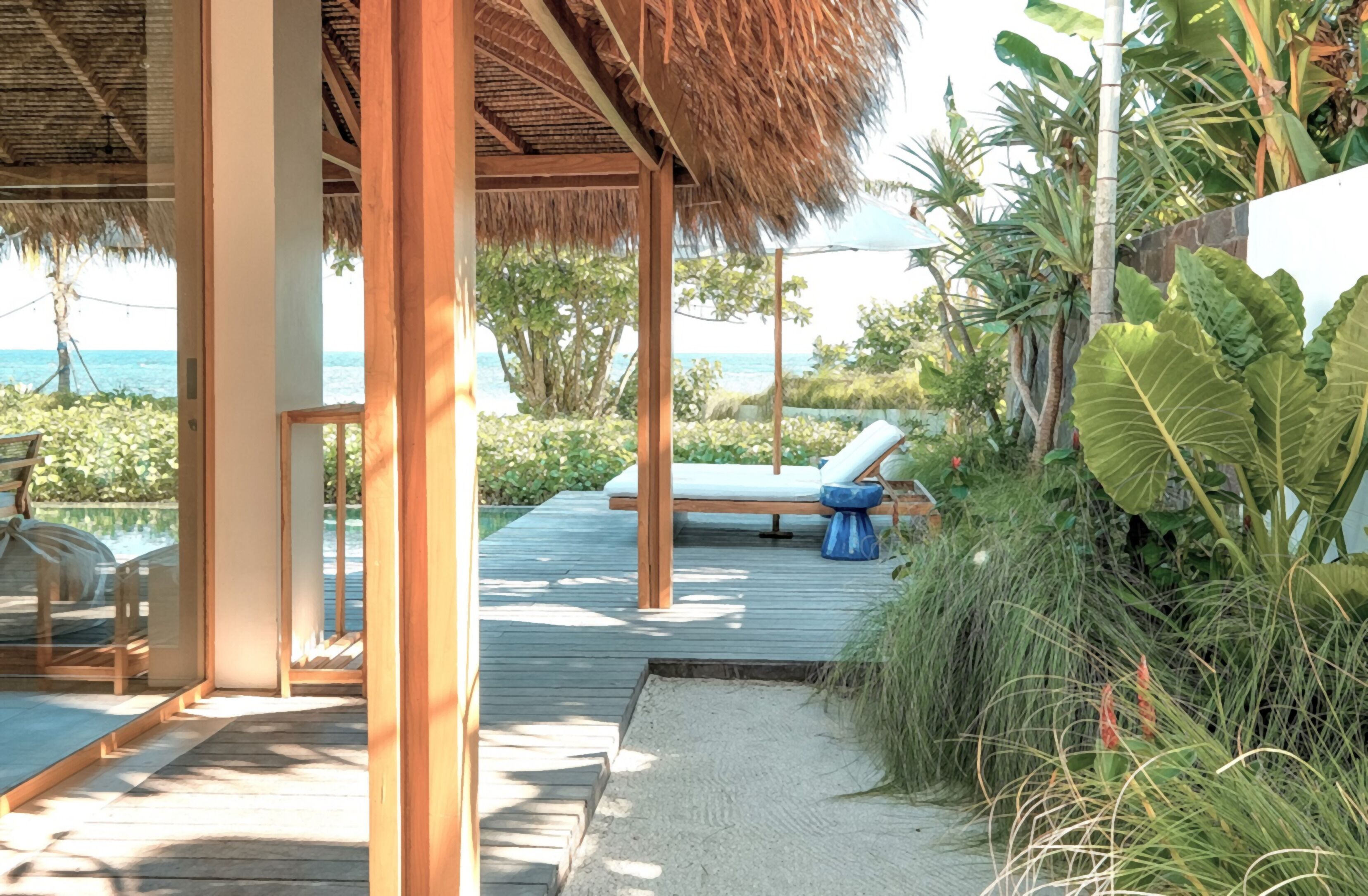 A wooden deck with a thatched roof, a lounge chair, and a view of the ocean.