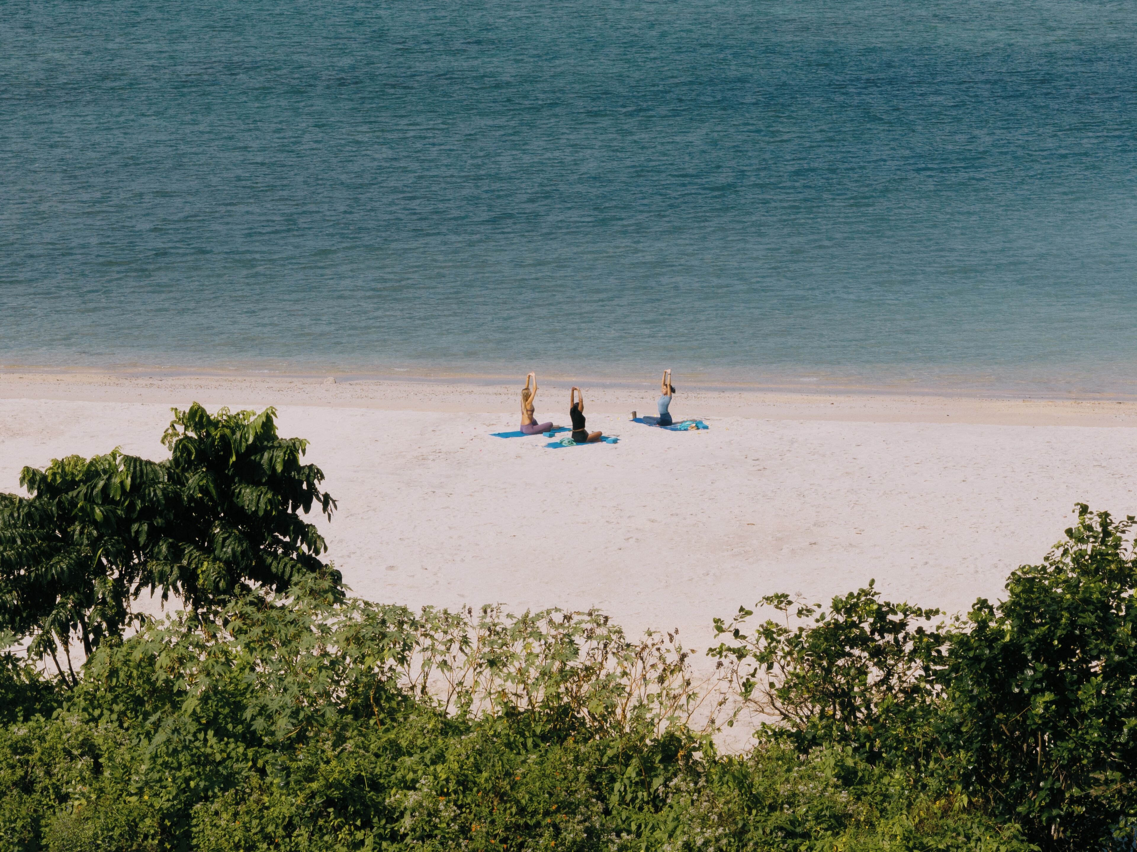 A beach with three people practicing yoga on mats.