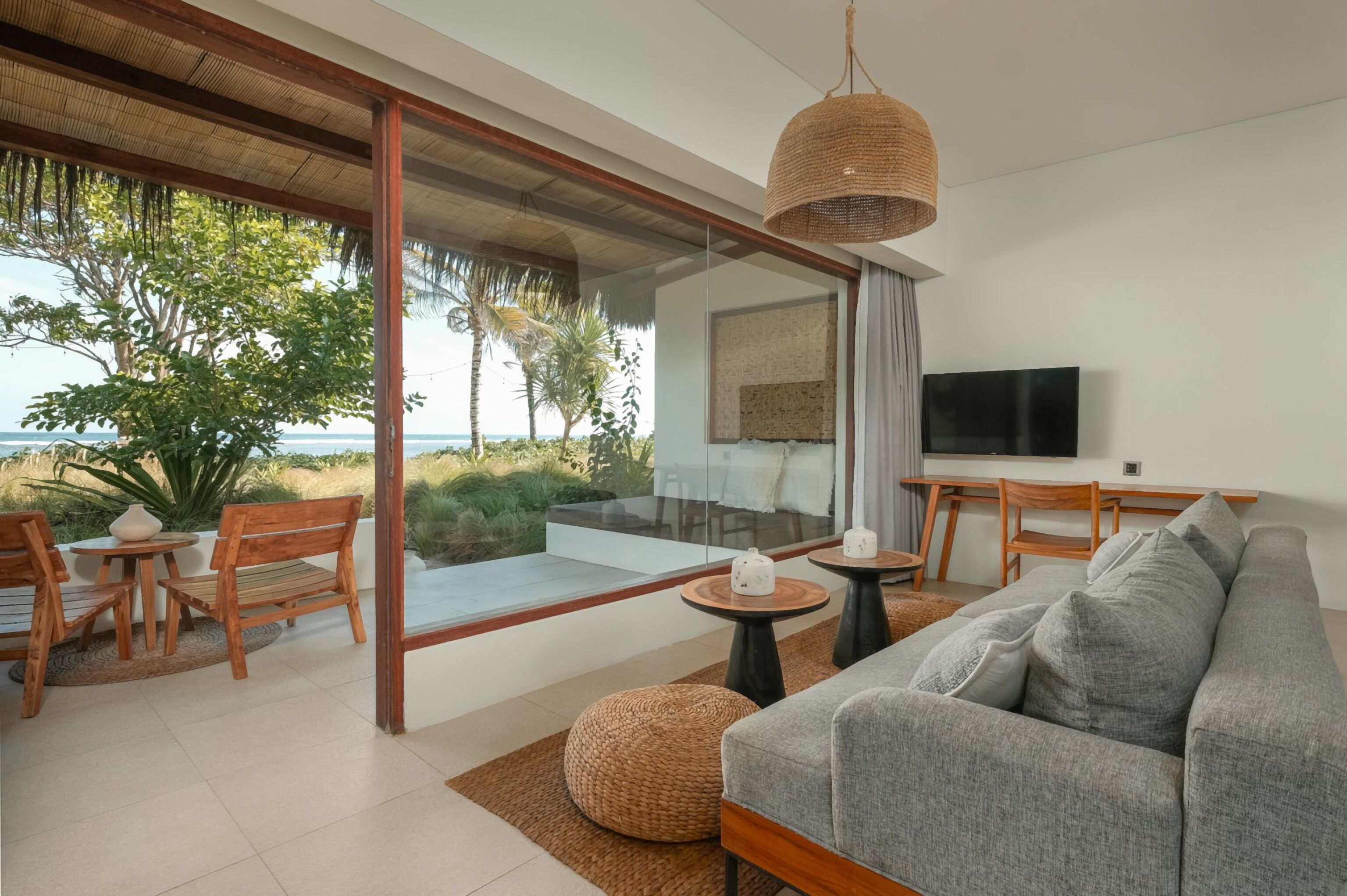 Een moderne woonkamer met een grijze bank, houten meubels, een televisie en uitzicht op de oceaan.