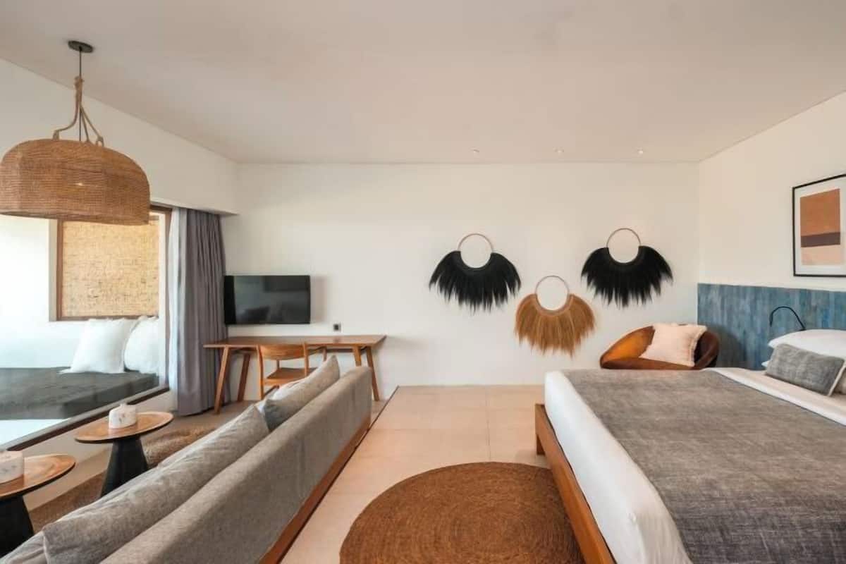 A modern hotel room with a sofa, a bed, a dining table, and a TV.