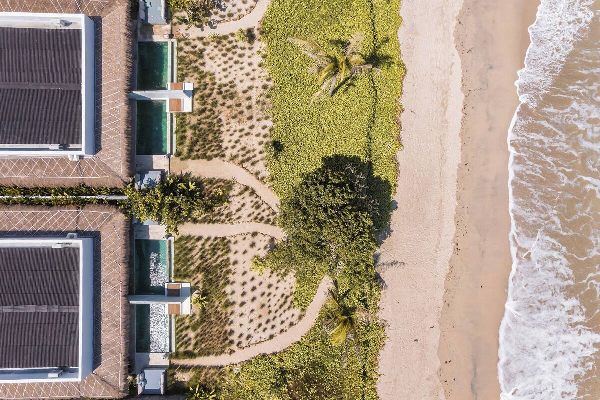 An aerial view of a beachfront property with two large buildings, a palm tree, and a sandy beach.
