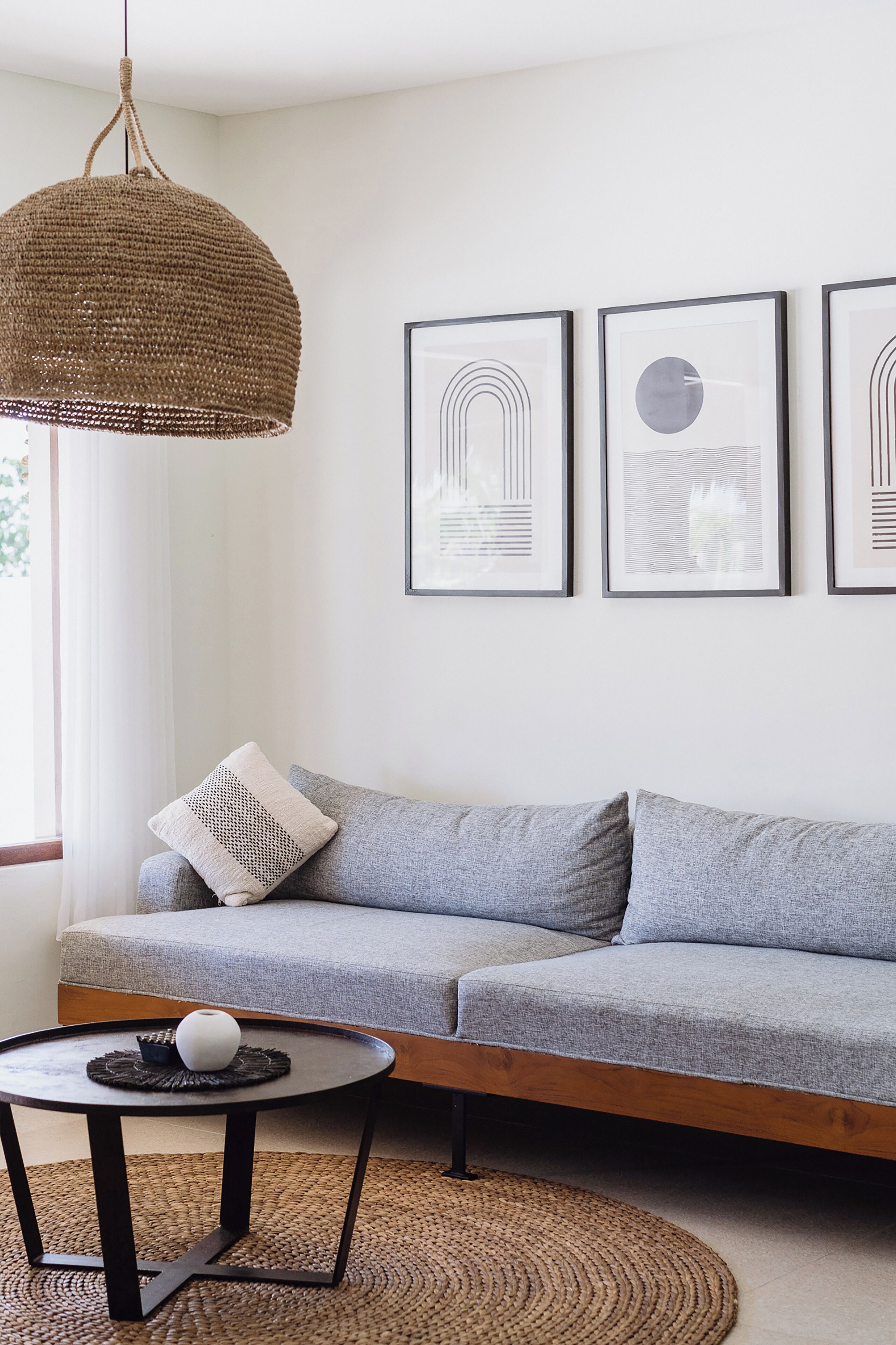 A modern living room with a grey sofa, a woven pendant light, a round coffee table, and framed artwork on the wall.
