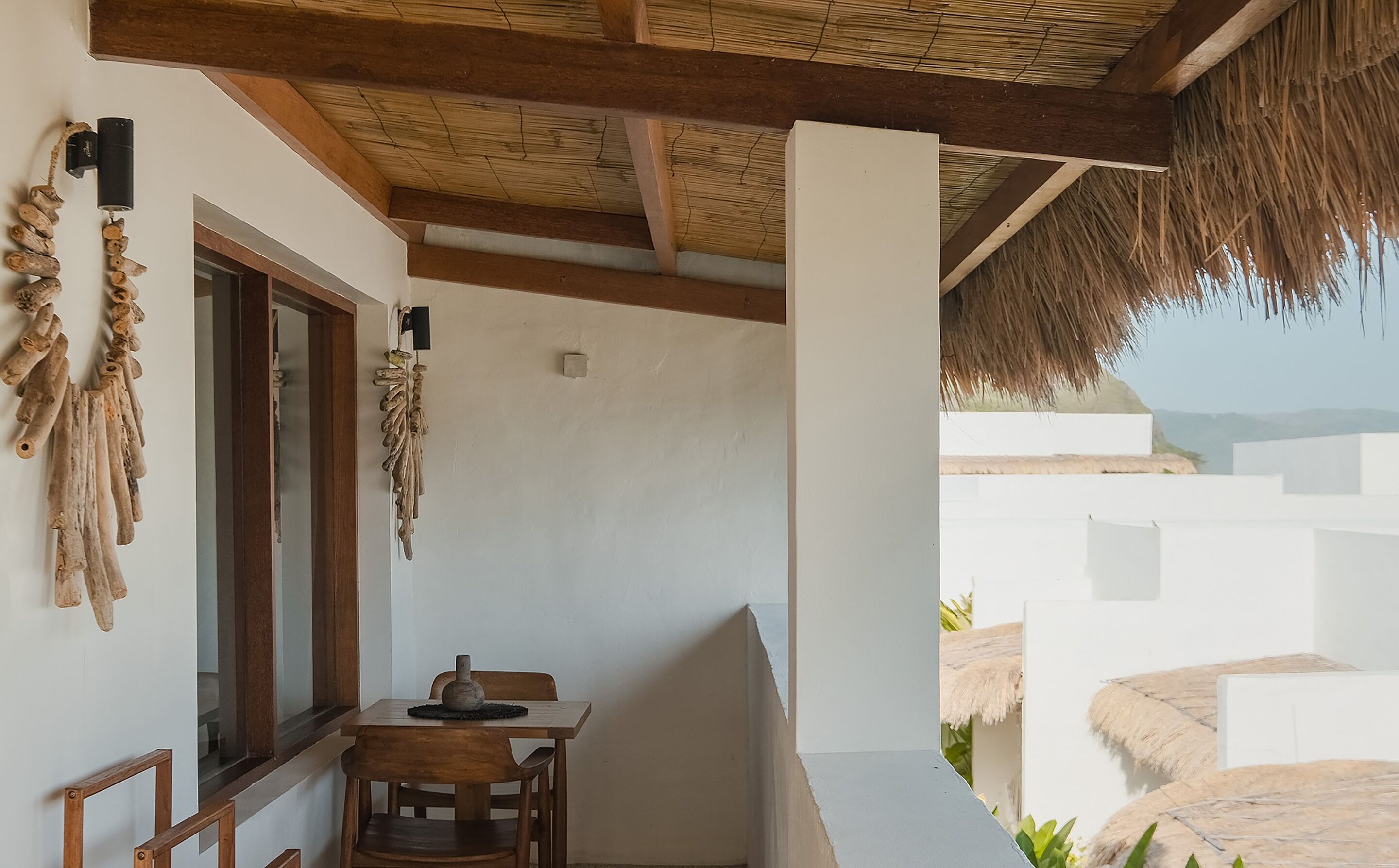 A room with a wooden table and chairs, a window, and a thatched roof.