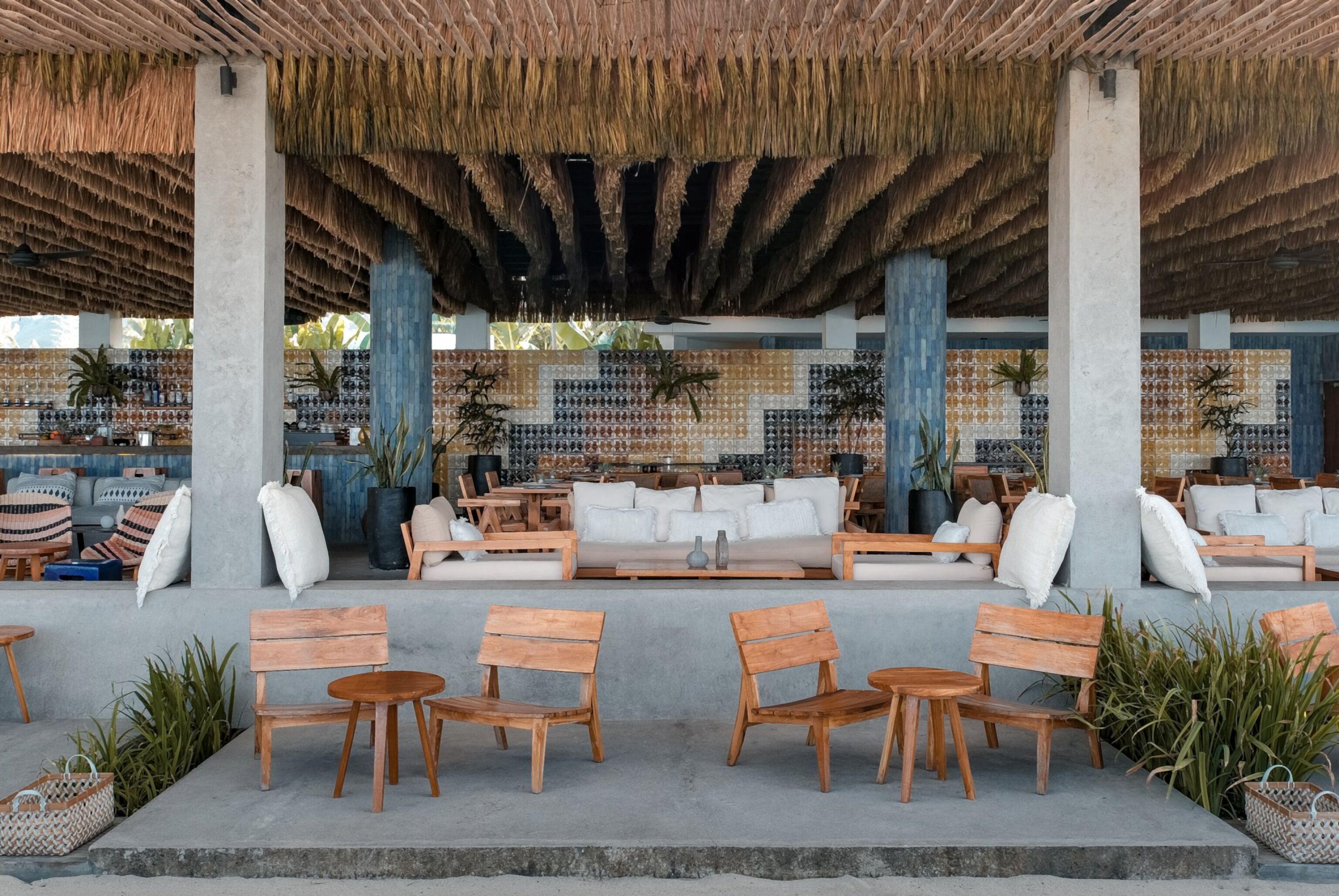 Un espace extérieur aménagé avec des meubles en bois, un toit de chaume et un mur orné de carreaux décoratifs.