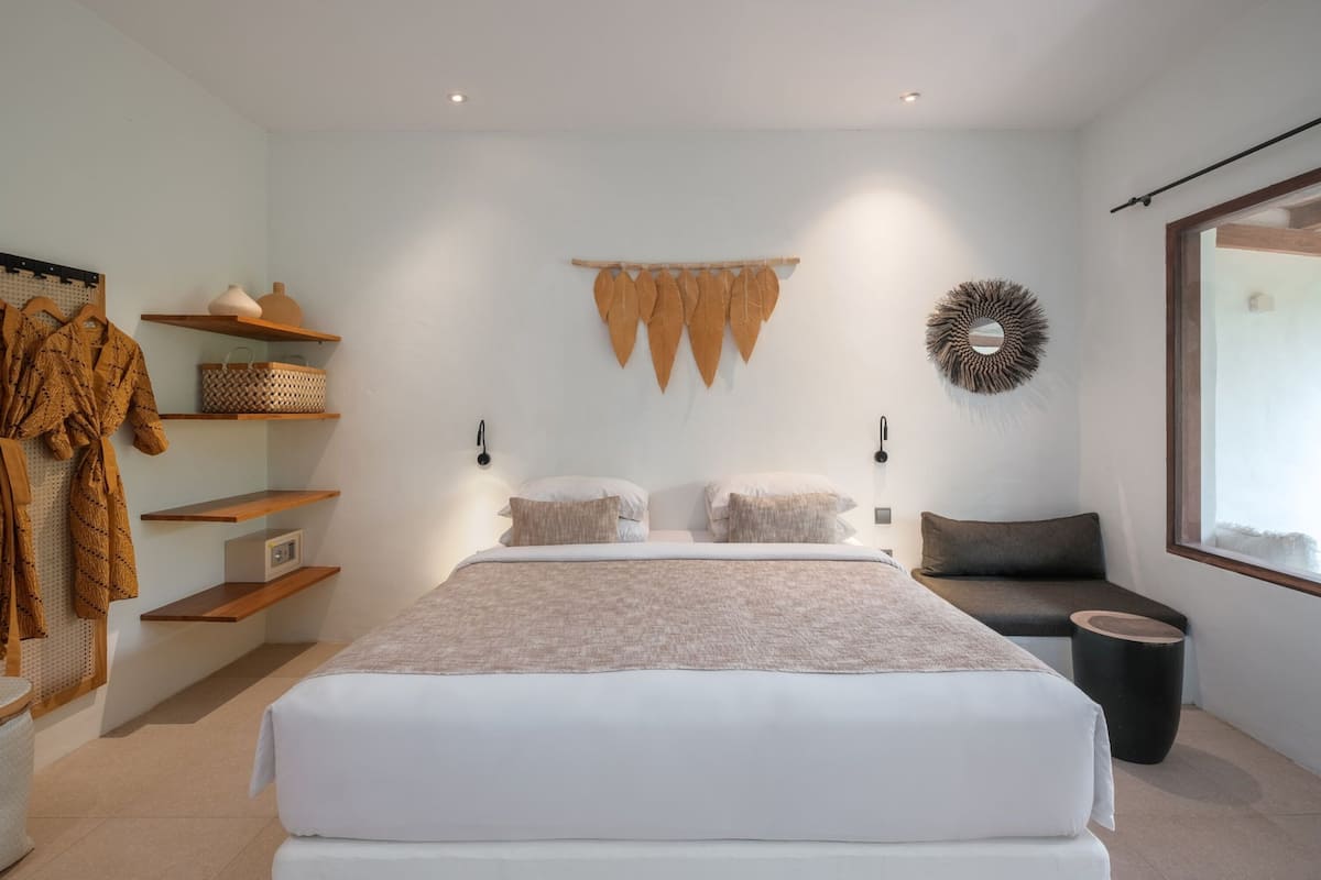 A modern bedroom with a large bed, built-in shelves, a seating area, and a decorative wall hanging.