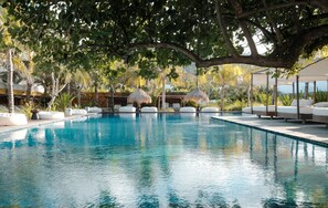 Una piscina con sillas de descanso y sombrillas, rodeada de árboles y un edificio al fondo.
