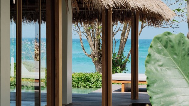 A wooden deck with a thatched roof structure, overlooking a clear blue sea.