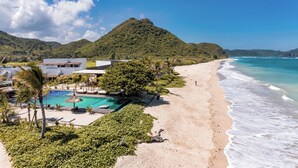 A beach resort with a swimming pool, palm trees, and a mountain in the background.